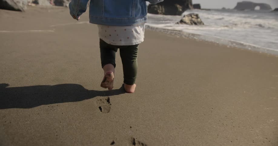 A small child without shoes is walking in the sand on the beach