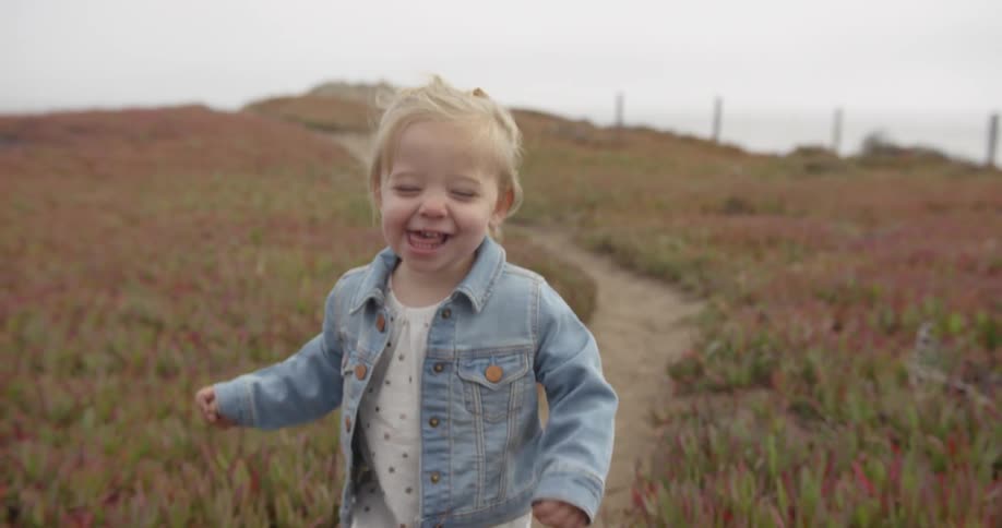 A little toddler girl is laughing as she walks down a dirt path