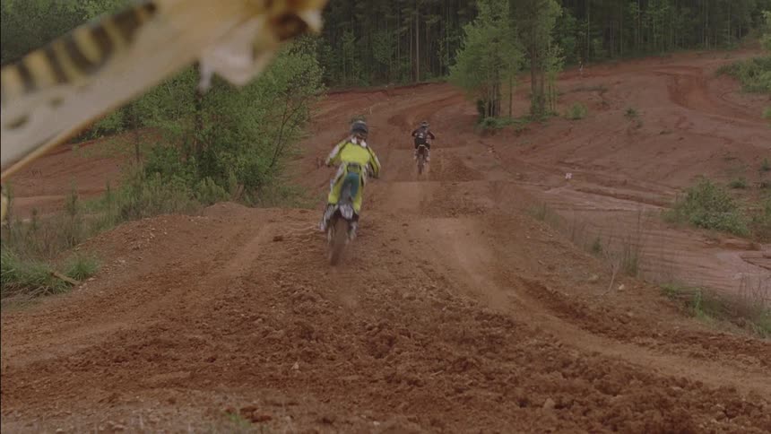 Racers ride dirt bikes on a bumpy muddy track