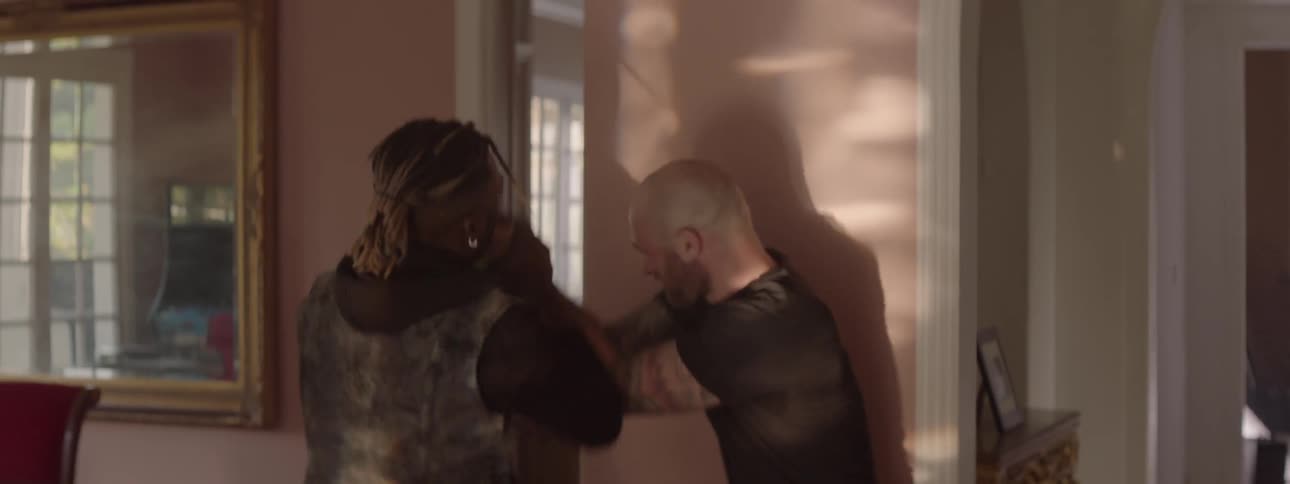 A man holding a gun inside a house begins fighting with another man