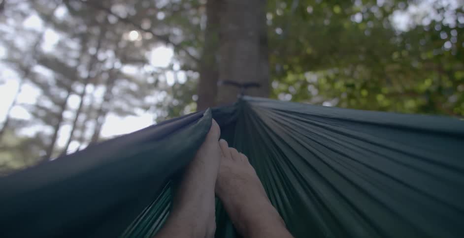 A man lying in a hammock is wiggling his feet during the day