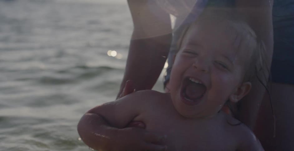 A baby laughs and smiles while being dunked the water