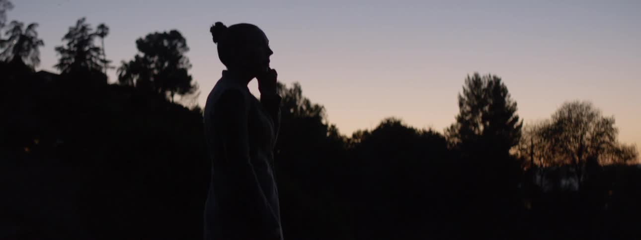 A woman talks on a phone outside at sunrise