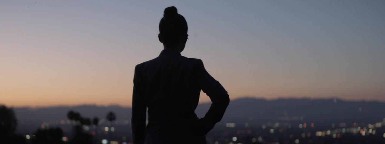 A woman looks out over a view at sunset