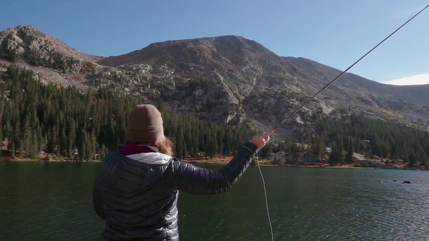 Woman stands on the edge of a lake and casts a fishing pole