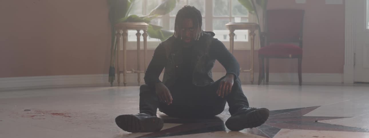 A man is sitting on the floor of a house out of breath and bleeding