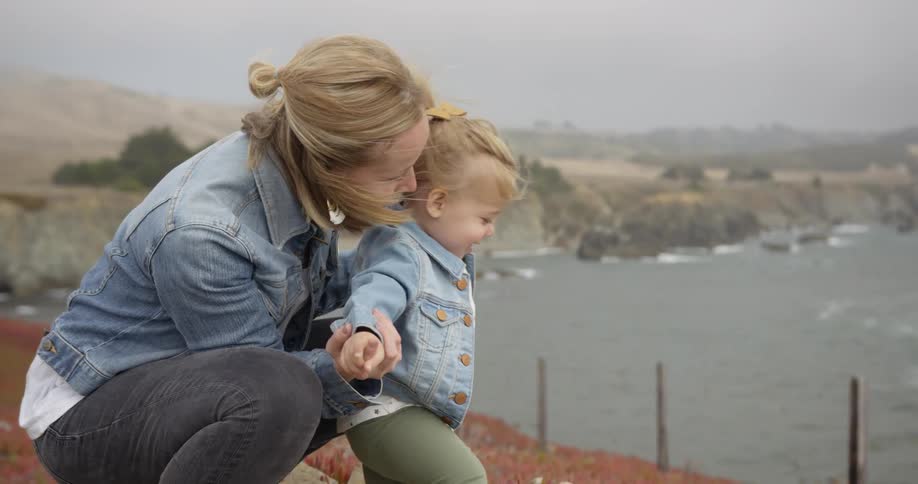 A woman kneels with a baby by the water