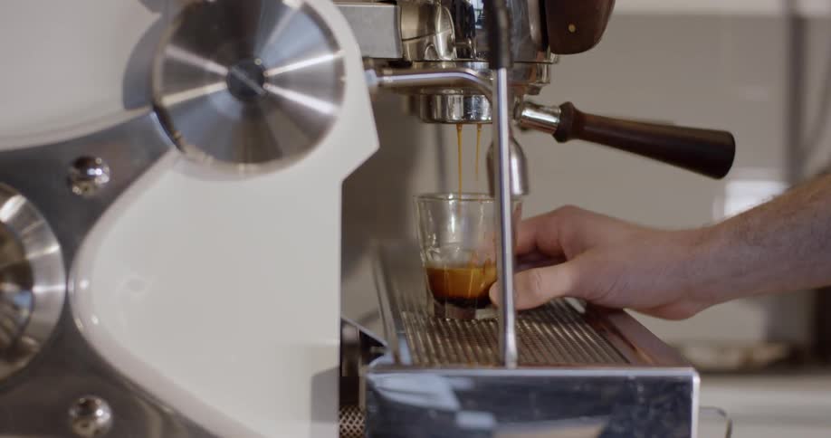 A man is making a glass of espresso at an espresso machine during the day