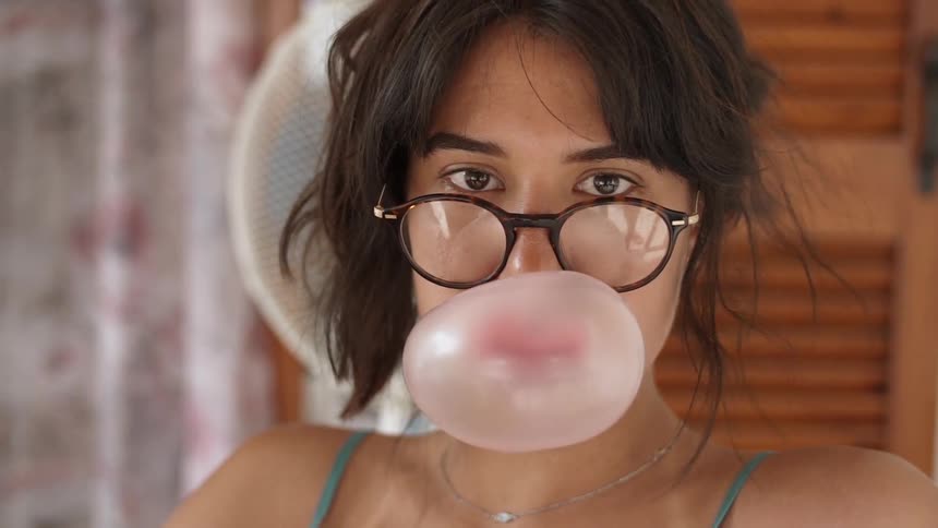 A woman is sitting outside and blowing bubble gum during the day