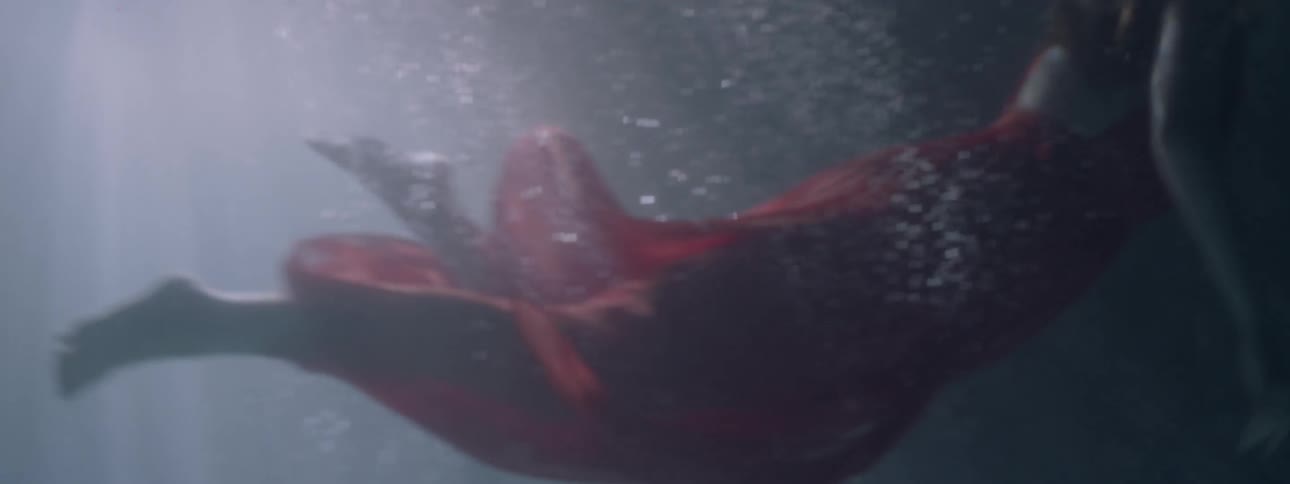 A woman dives into the water while wearing a red dress