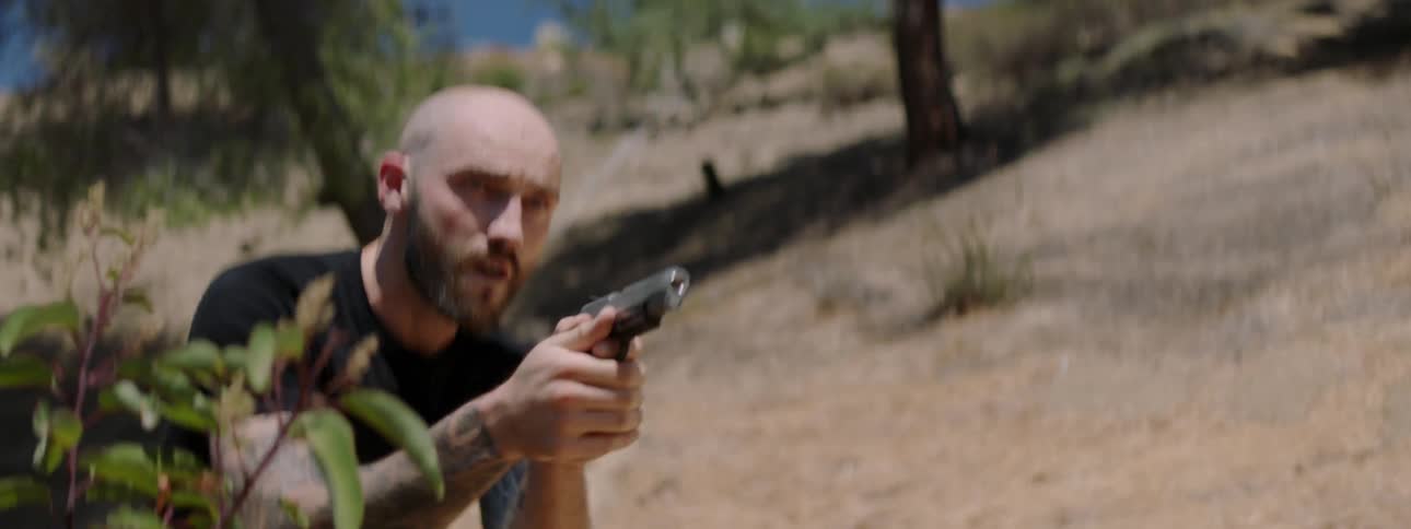 A man with a gun out and aimed makes his way down a hill