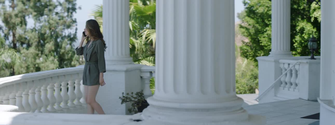 A woman is walking around the porch of a large white house