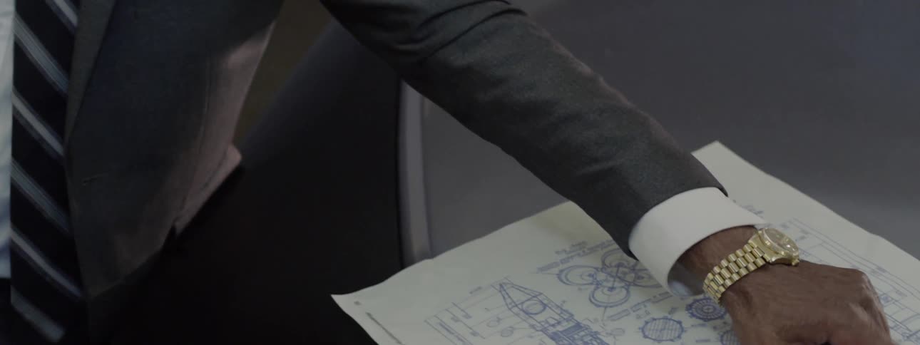 A man points at blueprints sitting on a car hood