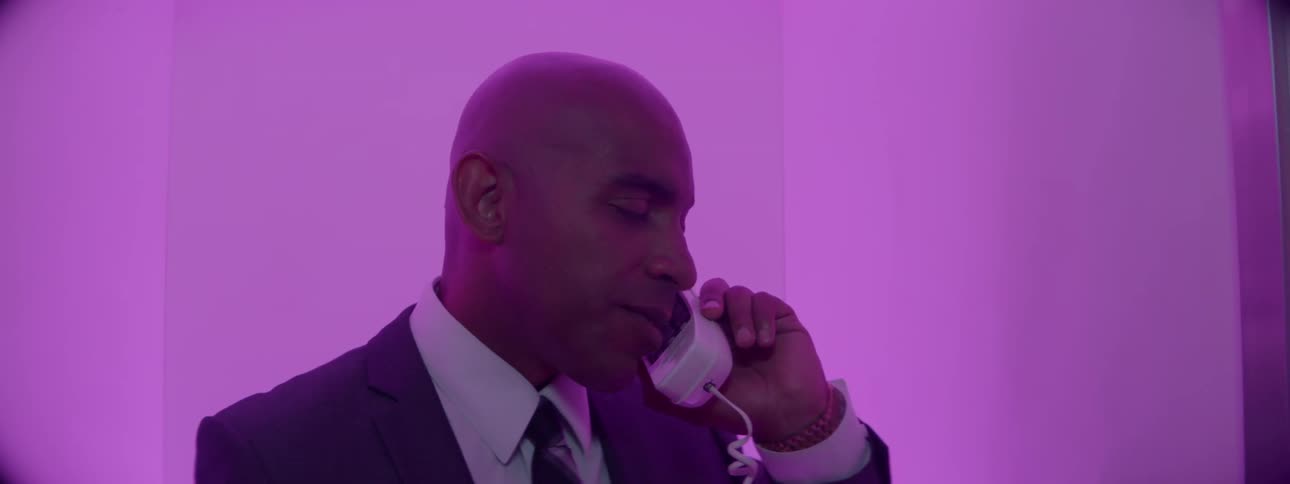 A man in a suit is using the telephone in a purple lit room