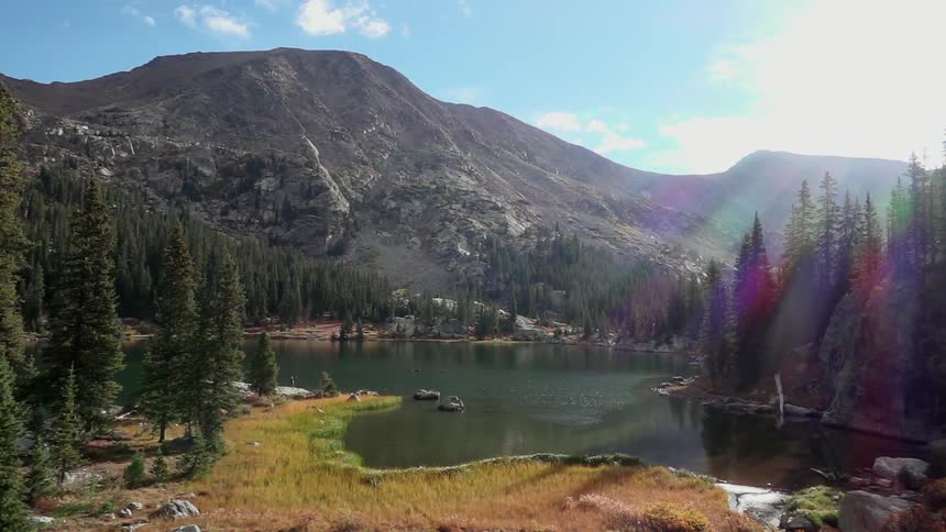Small lake surrounded by forest trees and mountains on sunny day