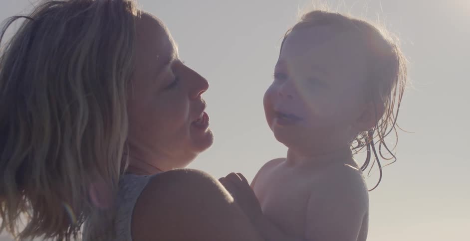 A woman kisses a baby and smiles on a sunny day