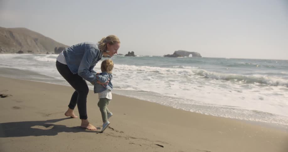 A mother walks with her young daughter on a sandy beach