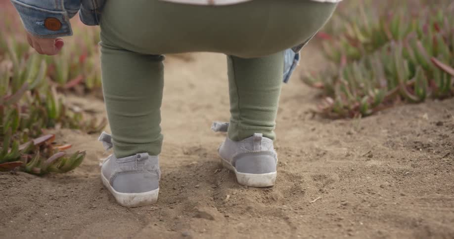 A toddler is using a rock to draw in the sand