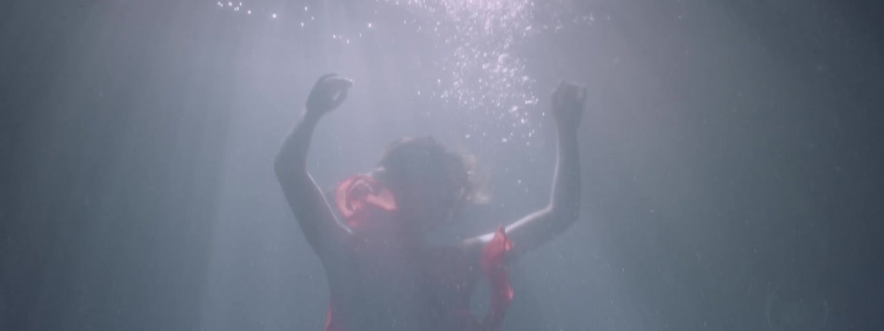 A woman in a red dress is sinking under the water during the day