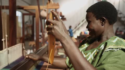 A smiling woman works at a loom