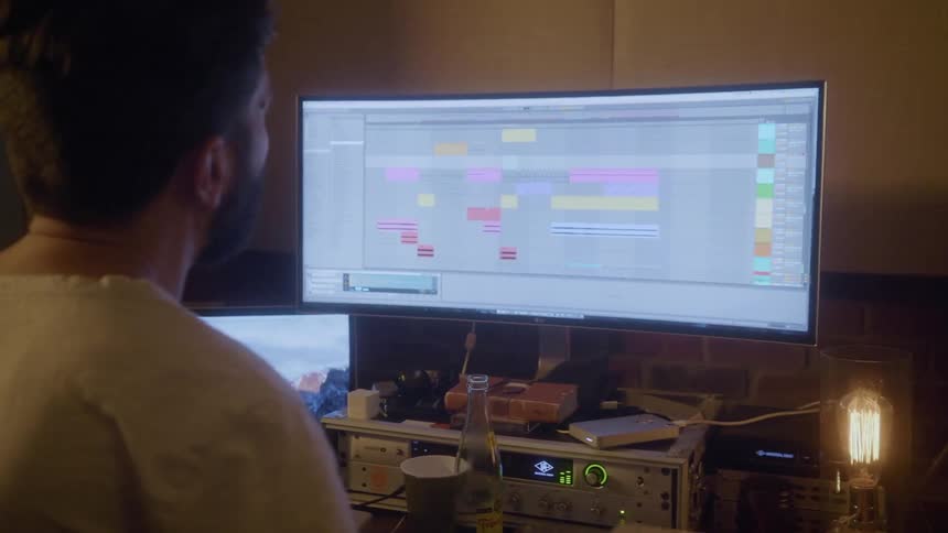 A man taps on a music pad then turns to his computer monitor