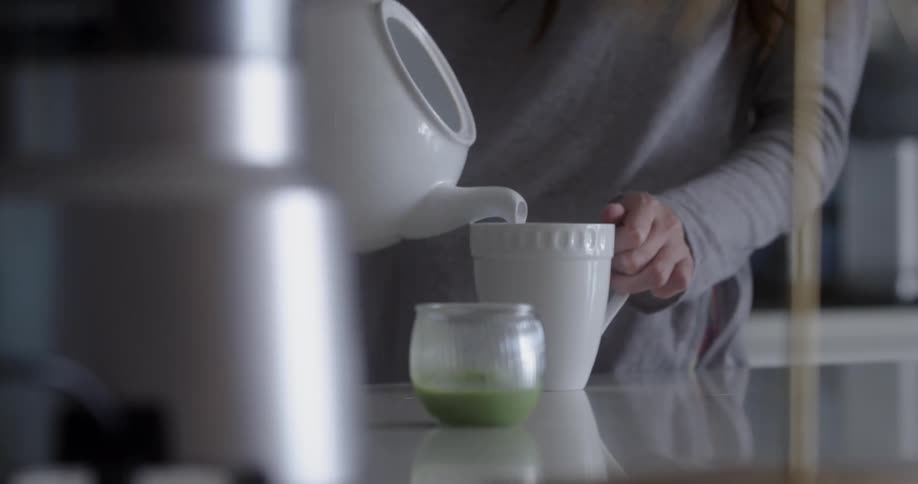 Woman pours hot water from a teapot into a mug