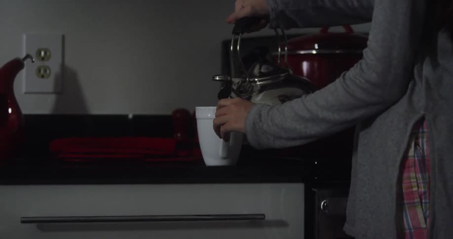 Woman lifts teapot from the stove and pours tea