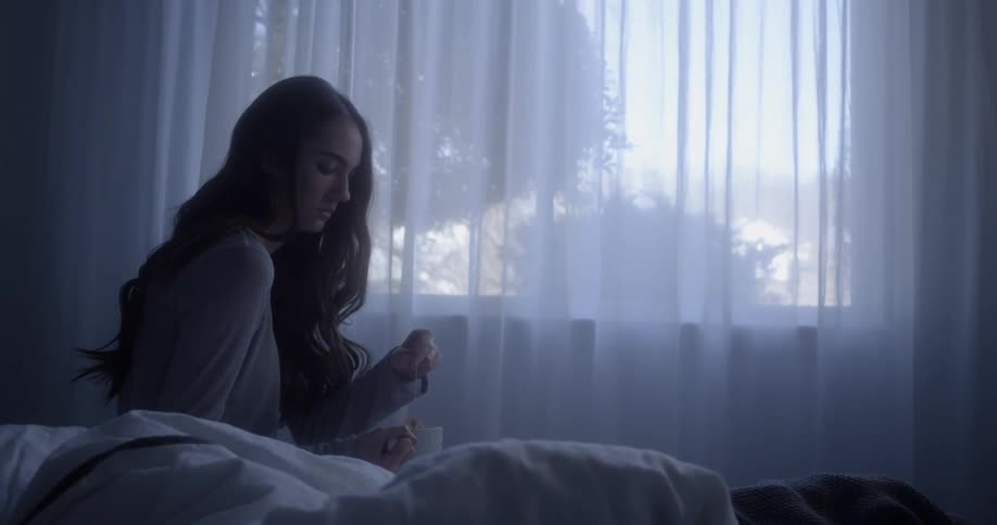 A woman is sitting up in bed with a cup of tea