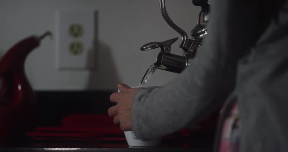 Woman pouring water from kettle into a mug in kitchen