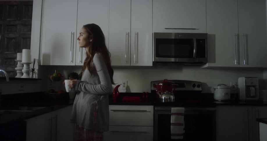 Woman holding a mug looks out her kitchen window