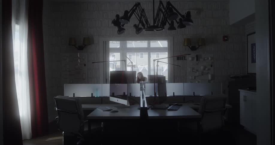 A woman is sitting in an office looking at computer monitors