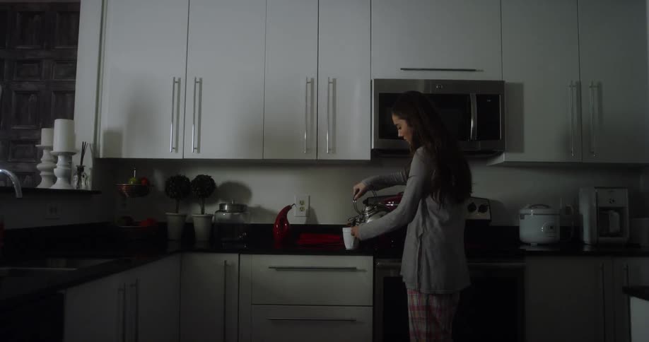 A woman is standing in the kitchen and she pours herself a cup of coffee