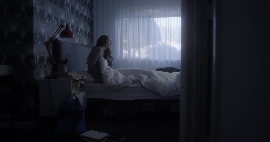 A woman is laying in bed and sets up and then gets out of bed