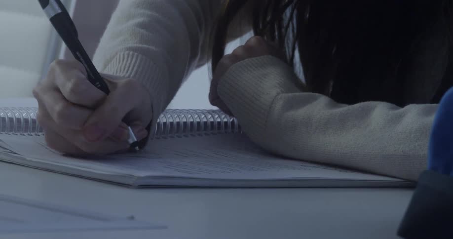 Woman sits at table and writes in notebook