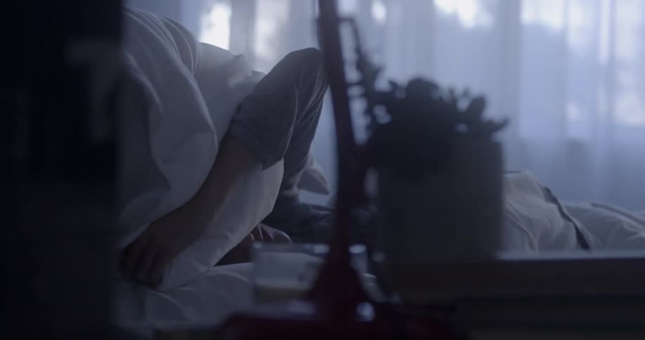 A woman lies in bed and puts a pillow on her face