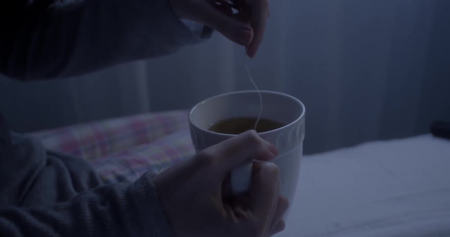 A woman dips a tea bag into a mug of water