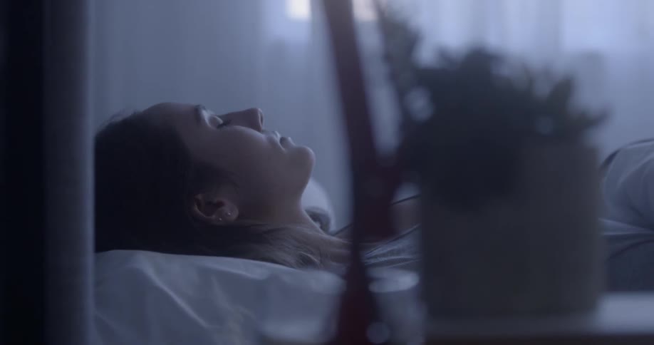Woman sits up from laying in bed on sunny day