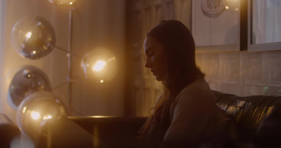 A woman is sitting in a dimly lit room reading a book