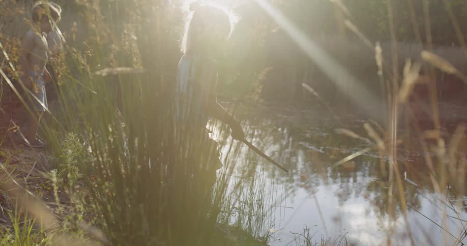Small children playing in pond water on sunny evening