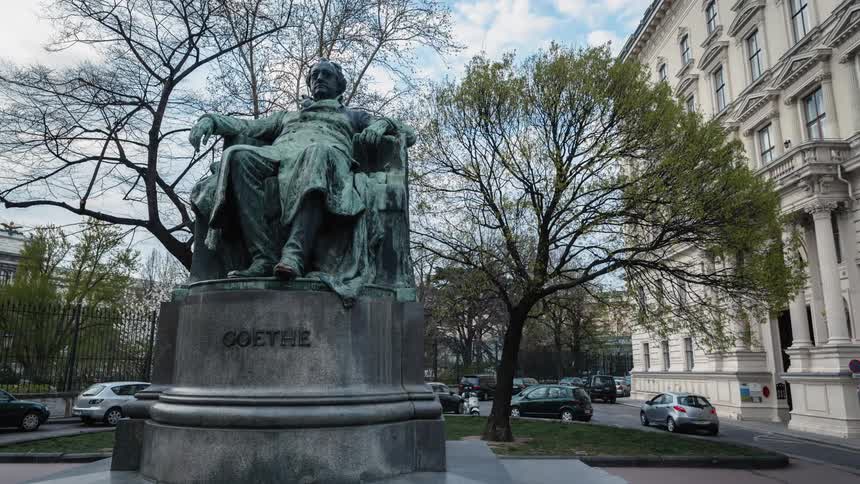 Time lapse footage of people walking around a statue of a man sitting in a chair