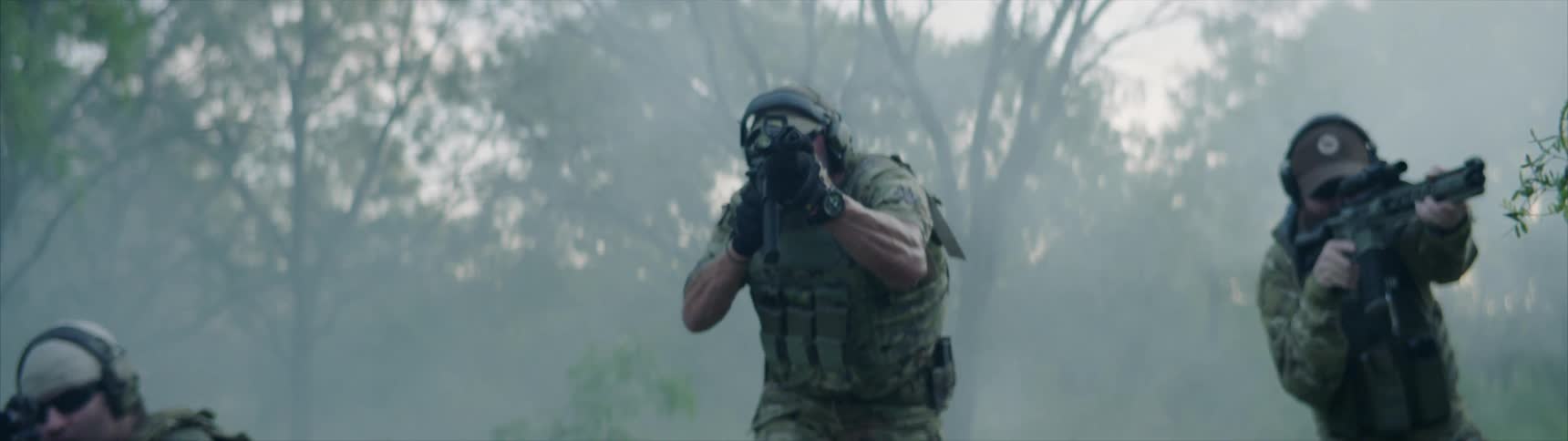 Soldiers with their guns drawn are walking towards the camera and one soldier fires a shot