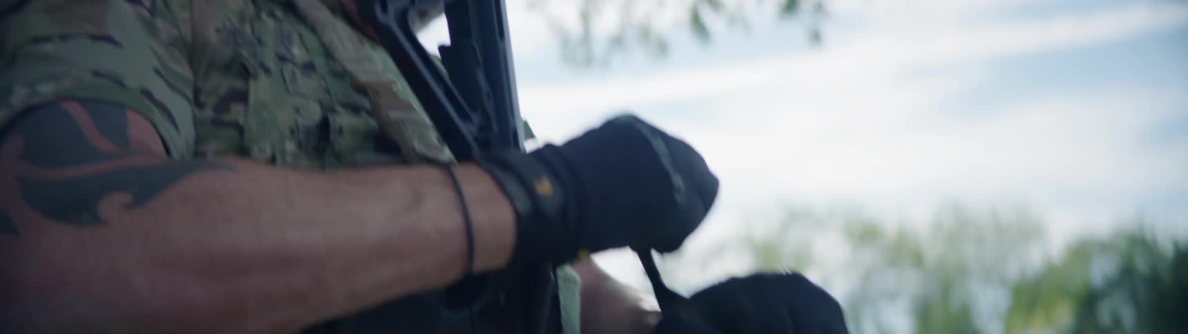 A man carrying a rifle puts on his gloves