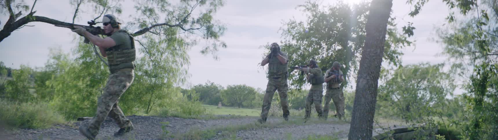 Army of men are aiming rifles as they walk over a bridge during the day