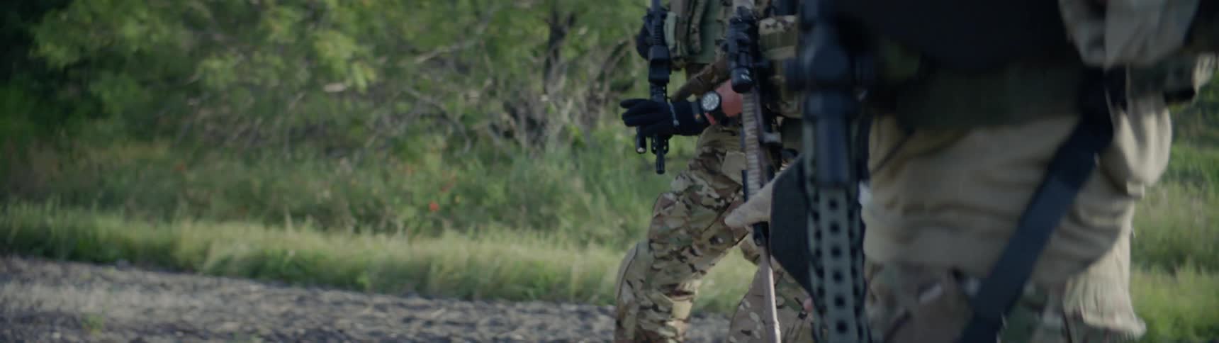 A combat unit is walking down a dirt road with guns