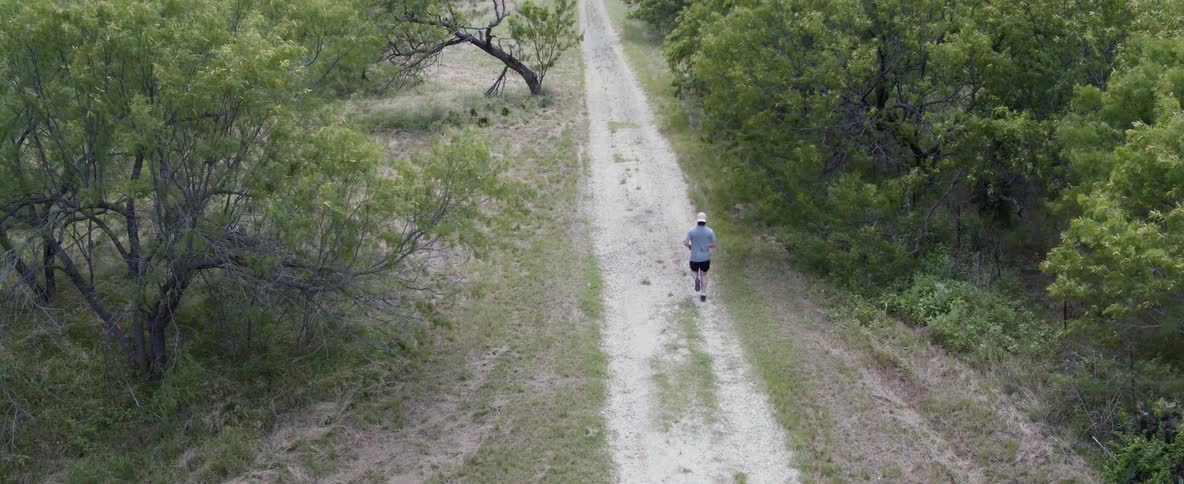 A man is jogging down a dirt road next to the woods