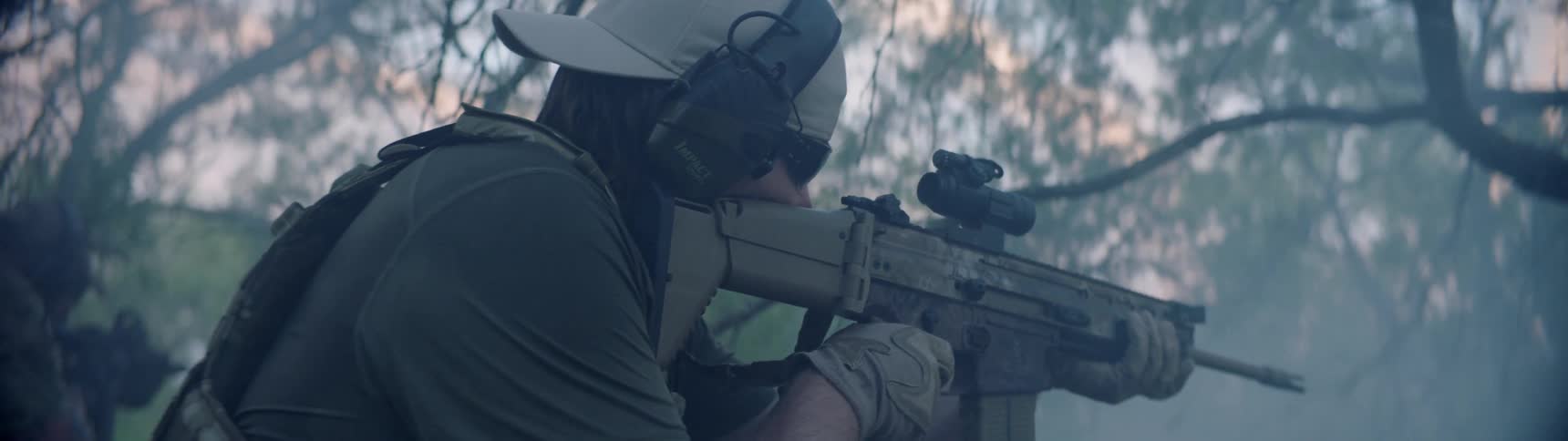Man holds machine gun and scans wooded area