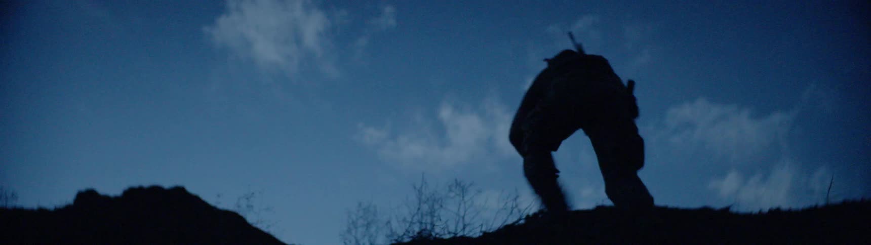 A man hikes up a hill carrying a rifle