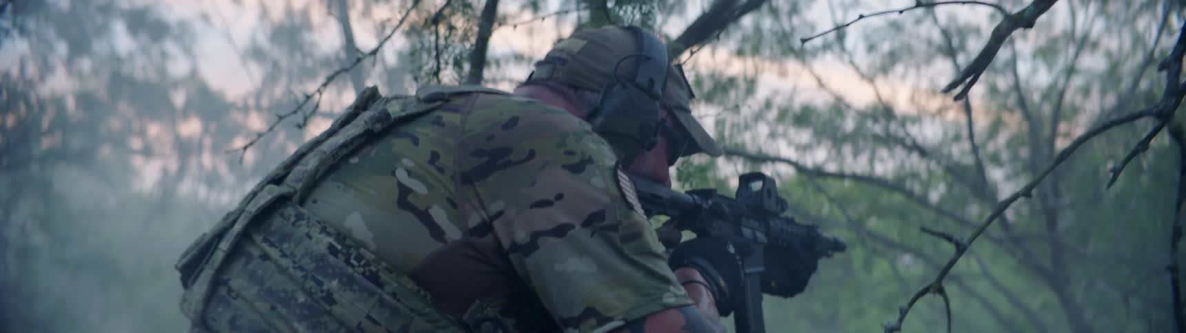 A man points his rifle ahead in the woods
