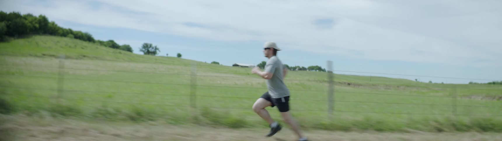 A man runs along a fenced field on a sunny day