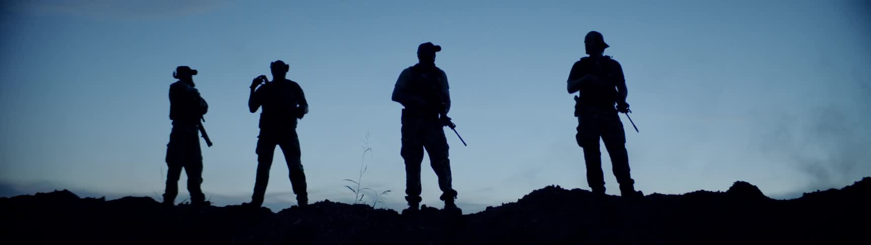 Three people with rifles stand on the hill